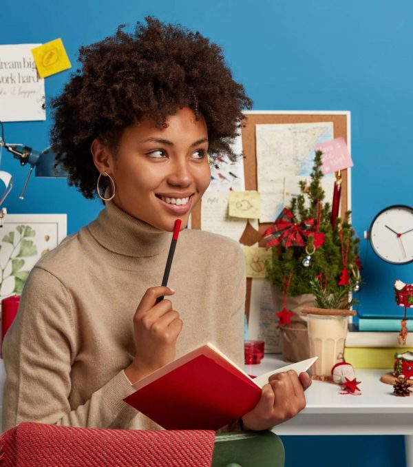 Dreamy positive student studies distantly during quarantine, sits near workplace, makes notes in diary, plans of preparation for exam, creats new poem, writes down text, tries to organize free time