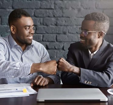 Business, teamwork and collaborataion concept. Two dark-skinned businesspeople in formal wear giving each other fist bump after successful agreement at meeting, happy with signing profitable contract Business, teamwork and collaborataion concept. Two dark-skinned businesspeople in formal wear giving each other fist bump after successful agreement at meeting, happy with signing profitable contract