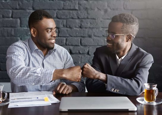 Business, teamwork and collaborataion concept. Two dark-skinned businesspeople in formal wear giving each other fist bump after successful agreement at meeting, happy with signing profitable contract