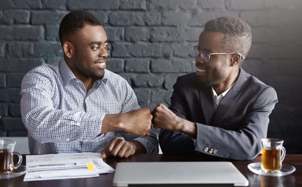 Business, teamwork and collaborataion concept. Two dark-skinned businesspeople in formal wear giving each other fist bump after successful agreement at meeting, happy with signing profitable contract Business, teamwork and collaborataion concept. Two dark-skinned businesspeople in formal wear giving each other fist bump after successful agreement at meeting, happy with signing profitable contract