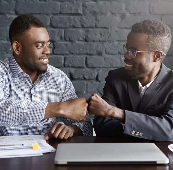 Business, teamwork and collaborataion concept. Two dark-skinned businesspeople in formal wear giving each other fist bump after successful agreement at meeting, happy with signing profitable contract