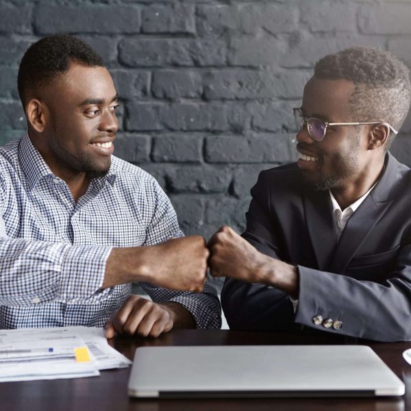 Business, teamwork and collaborataion concept. Two dark-skinned businesspeople in formal wear giving each other fist bump after successful agreement at meeting, happy with signing profitable contract Business, teamwork and collaborataion concept. Two dark-skinned businesspeople in formal wear giving each other fist bump after successful agreement at meeting, happy with signing profitable contract