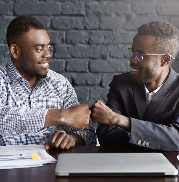 Business, teamwork and collaborataion concept. Two dark-skinned businesspeople in formal wear giving each other fist bump after successful agreement at meeting, happy with signing profitable contract